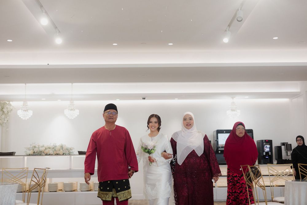 A bride in a white gown poses with family in traditional Malay attire at an elegant wedding venue.