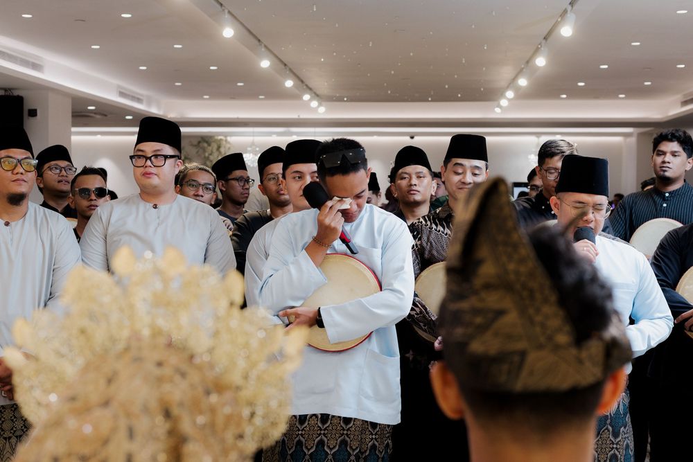 Men in traditional Malay attire playing rebana drums during a cultural ceremony indoors.