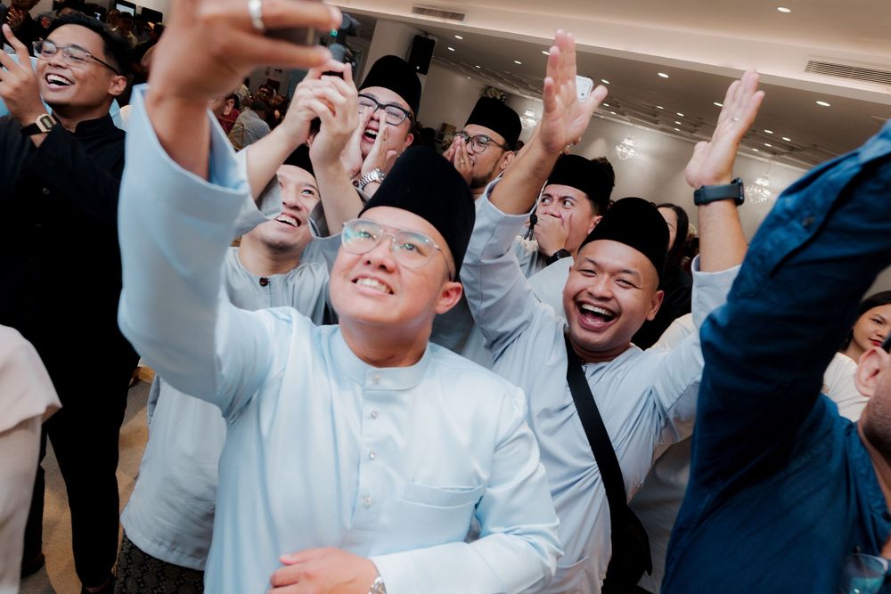 Group of men in traditional Malay attire taking a joyful selfie at a festive celebration.
