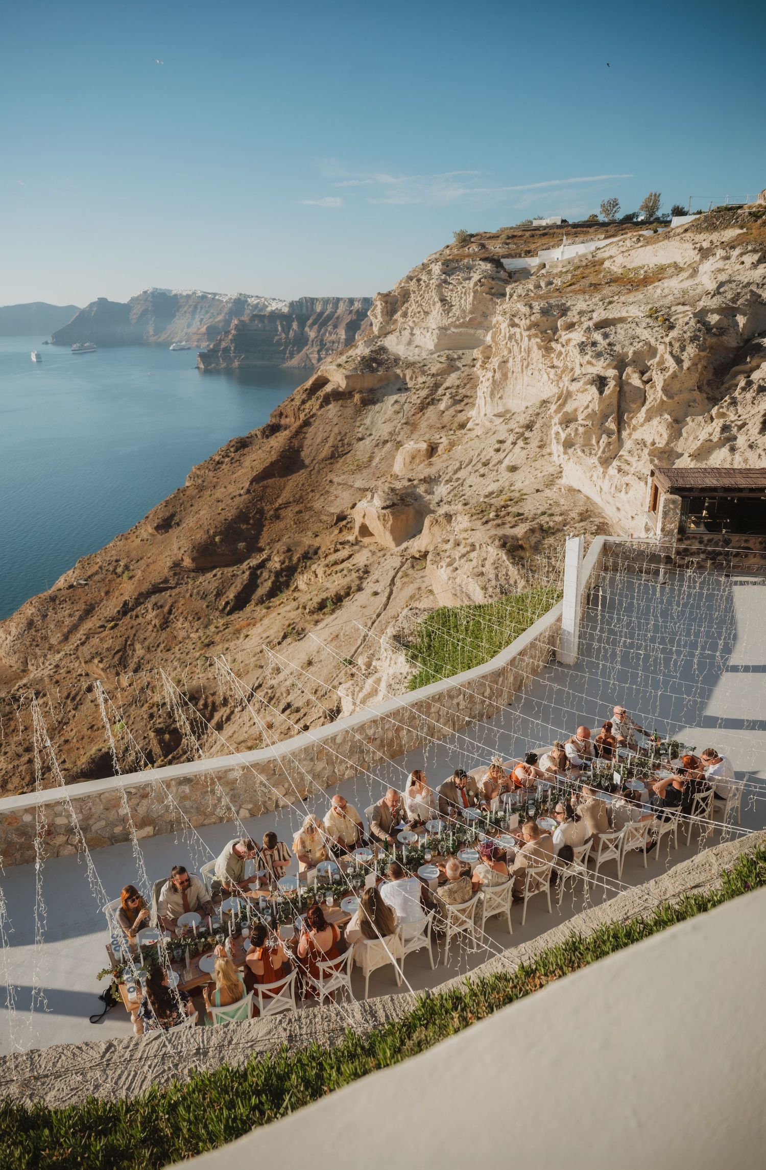 Outdoor cliffside dining event in Santorini, Greece, with guests seated at long tables overlooking the caldera.