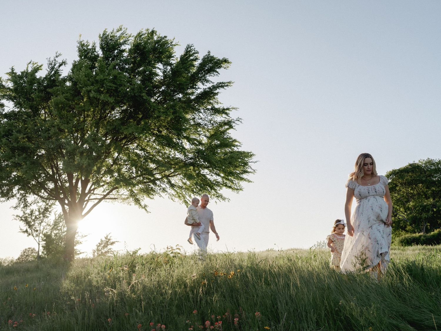 Family walking through a meadow beside a large oak tree at golden hour in Dallas