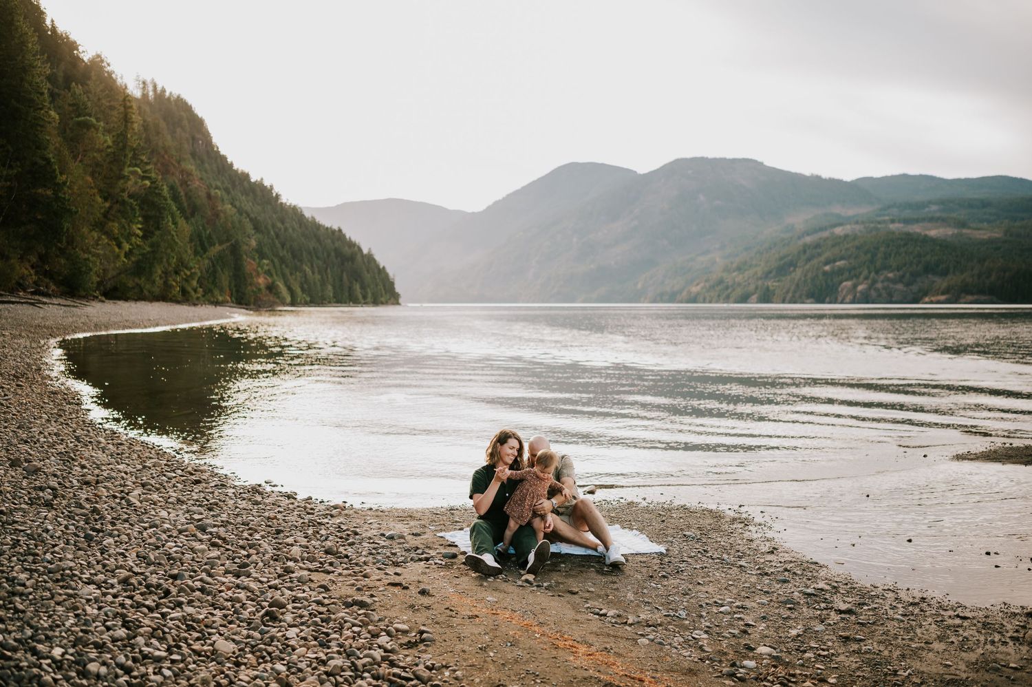 Comox Valley Photographer Portraits at Comox Lake in Cumberland, Vancouver Island. Family sitting on blanket in front of lake and mountains