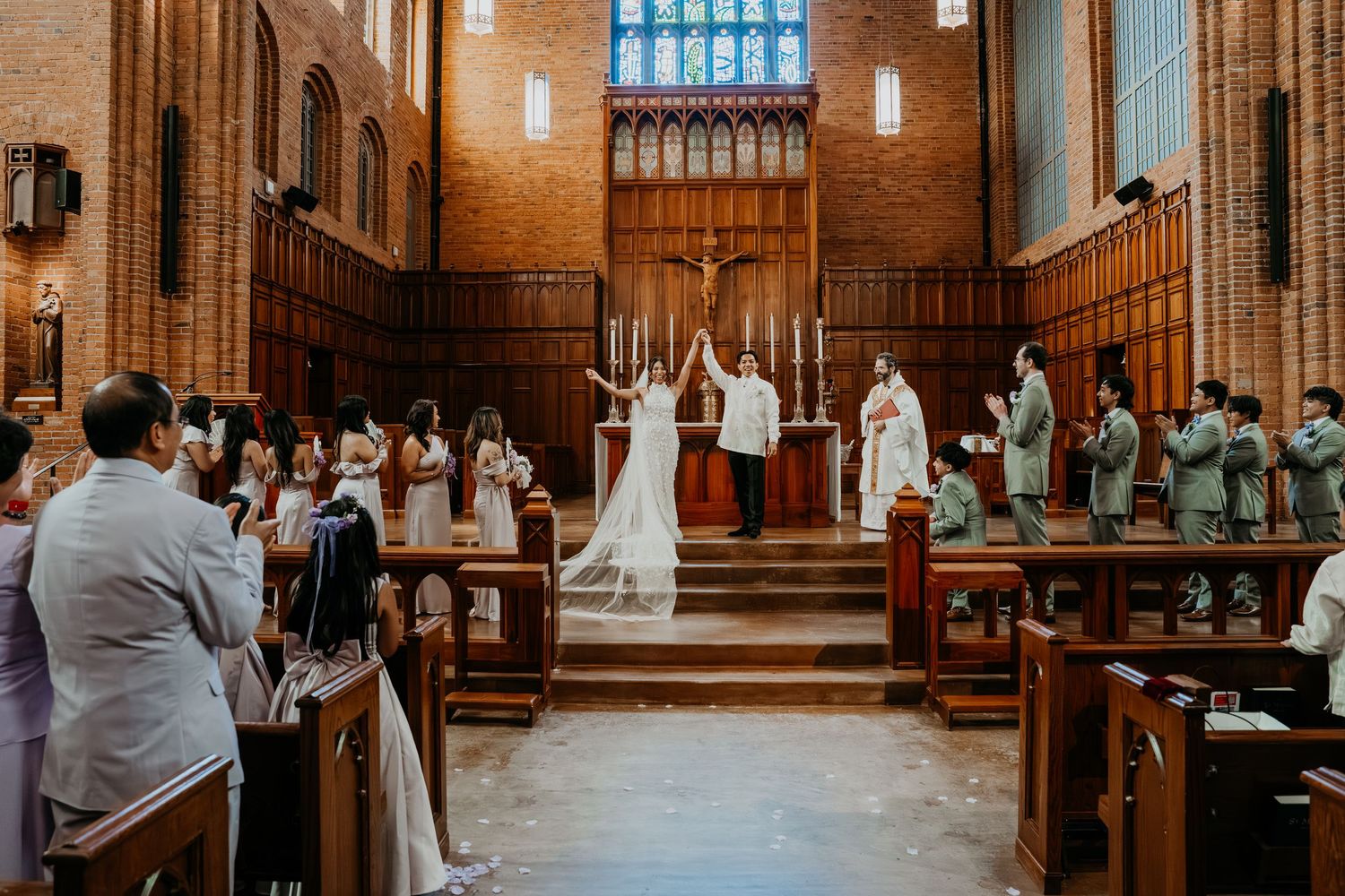 Asian bride and groom holding hands up in the air as they were just pronounced husband and wife at a catholic church in seattle, wa.
