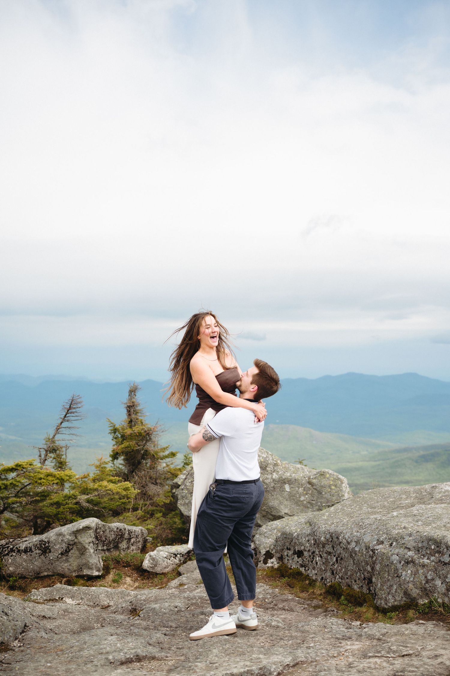 Man lifting joyful woman on rocky mountain top with panoramic views.