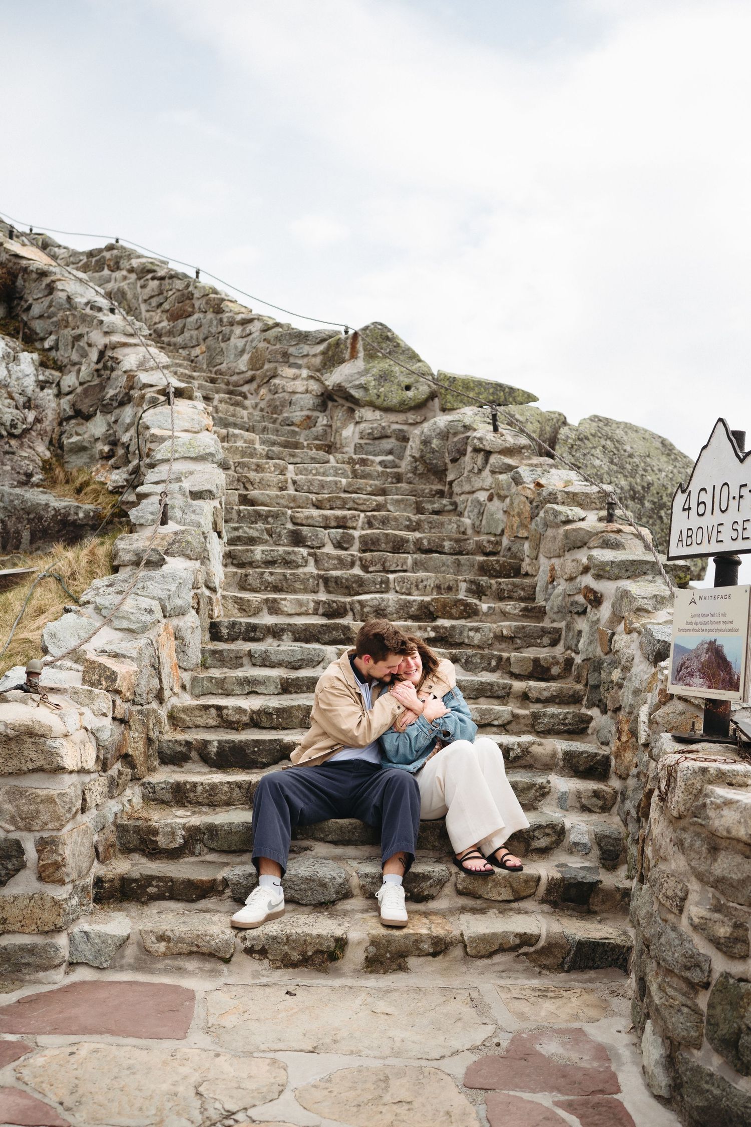 Couple sitting close together on rustic stone steps at 4610 feet above sea level overlook on a cloudy day.