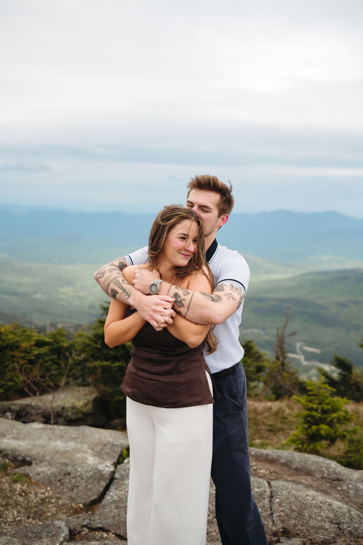 Happy couple embracing on mountain top with stunning green valley backdrop.