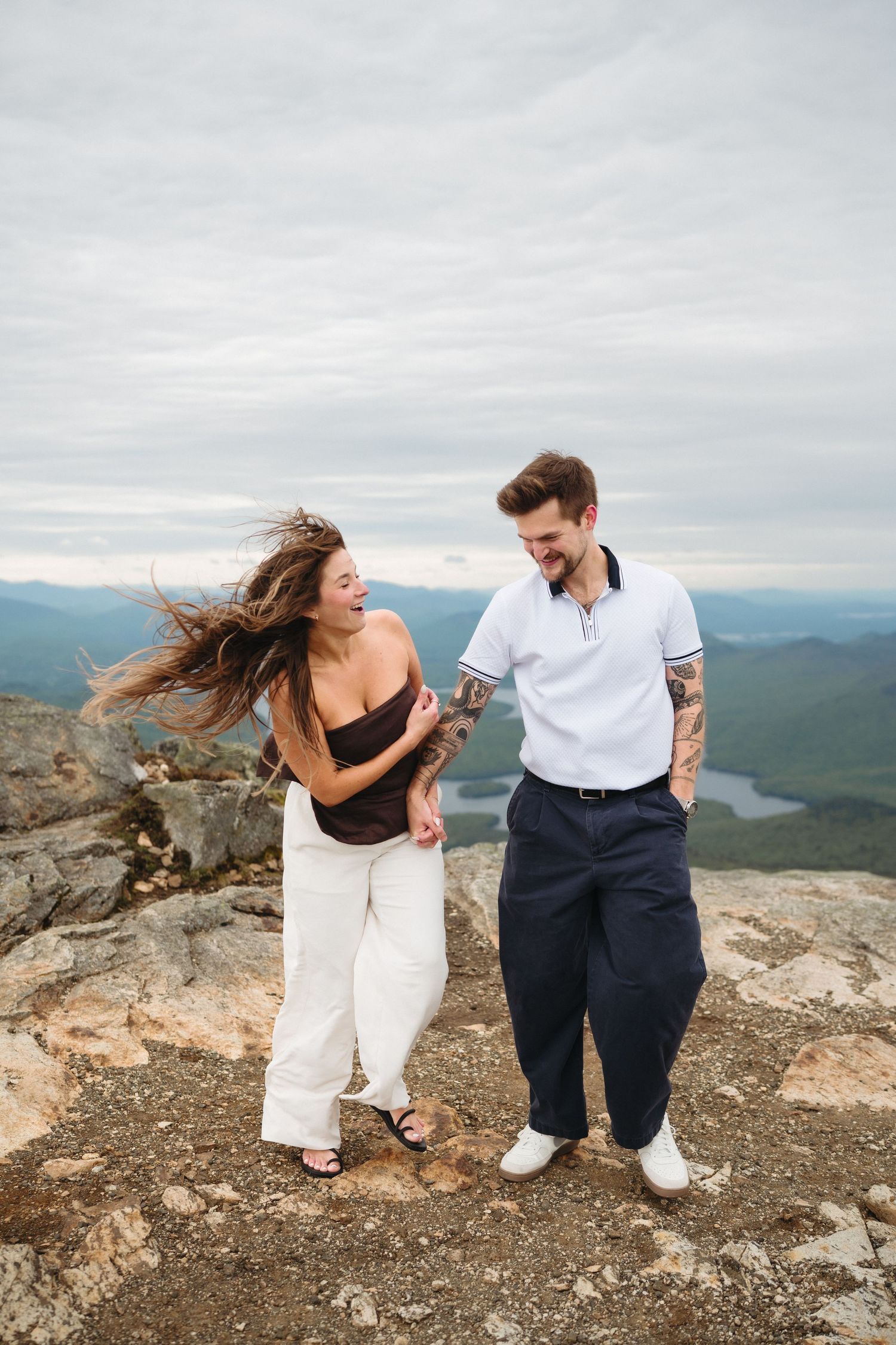 Laughing couple walking on mountain summit with wind blowing womans hair.