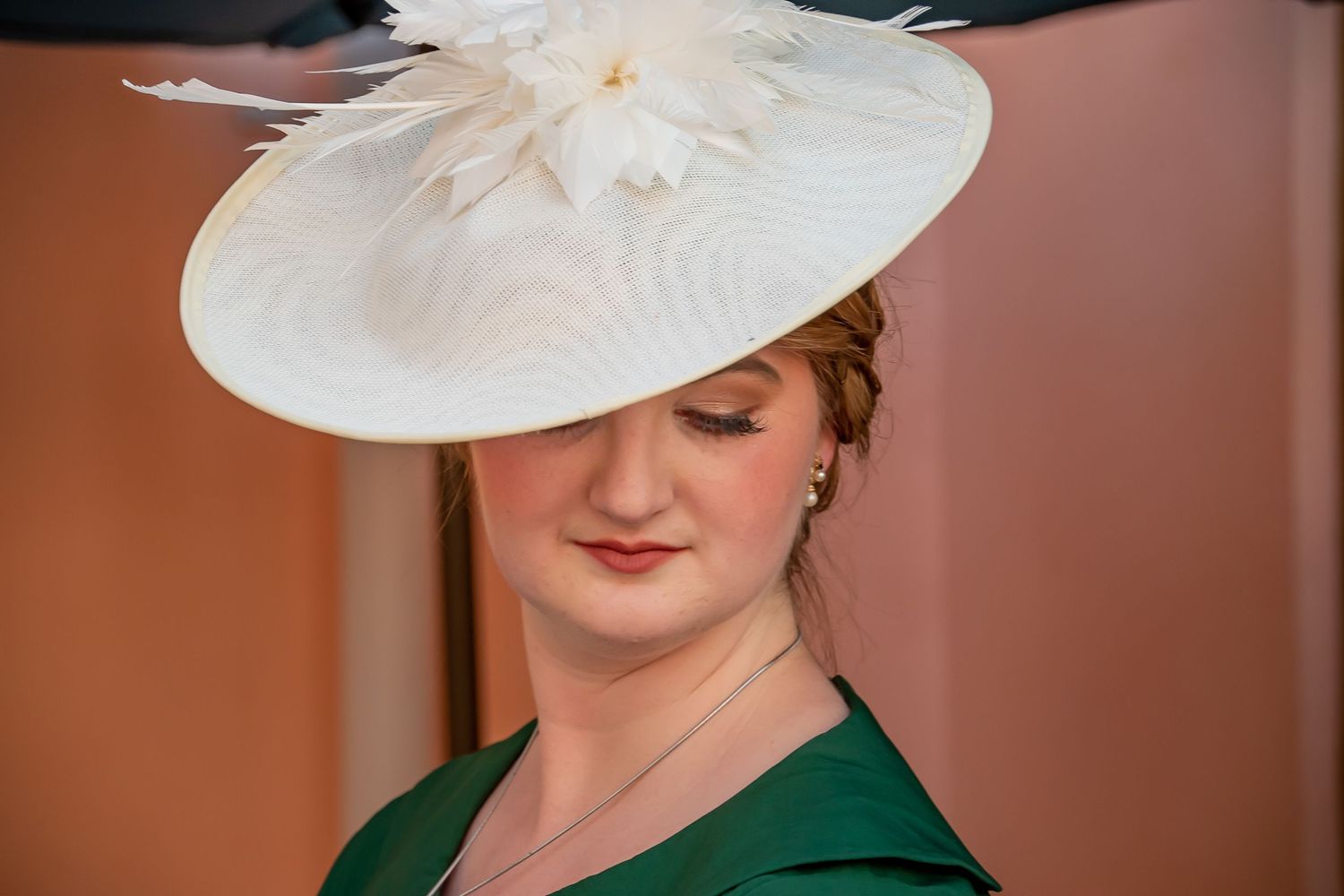 Woman in elegant green dress wearing a large white fascinator hat with feathers at a formal event.