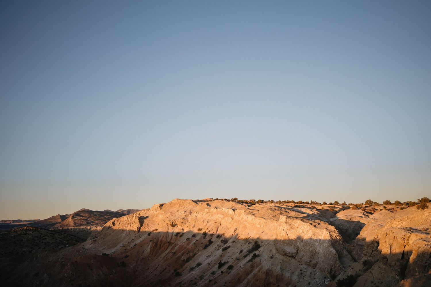 Rugged desert rock formations bathed in warm golden sunset light against a clear blue sky.
