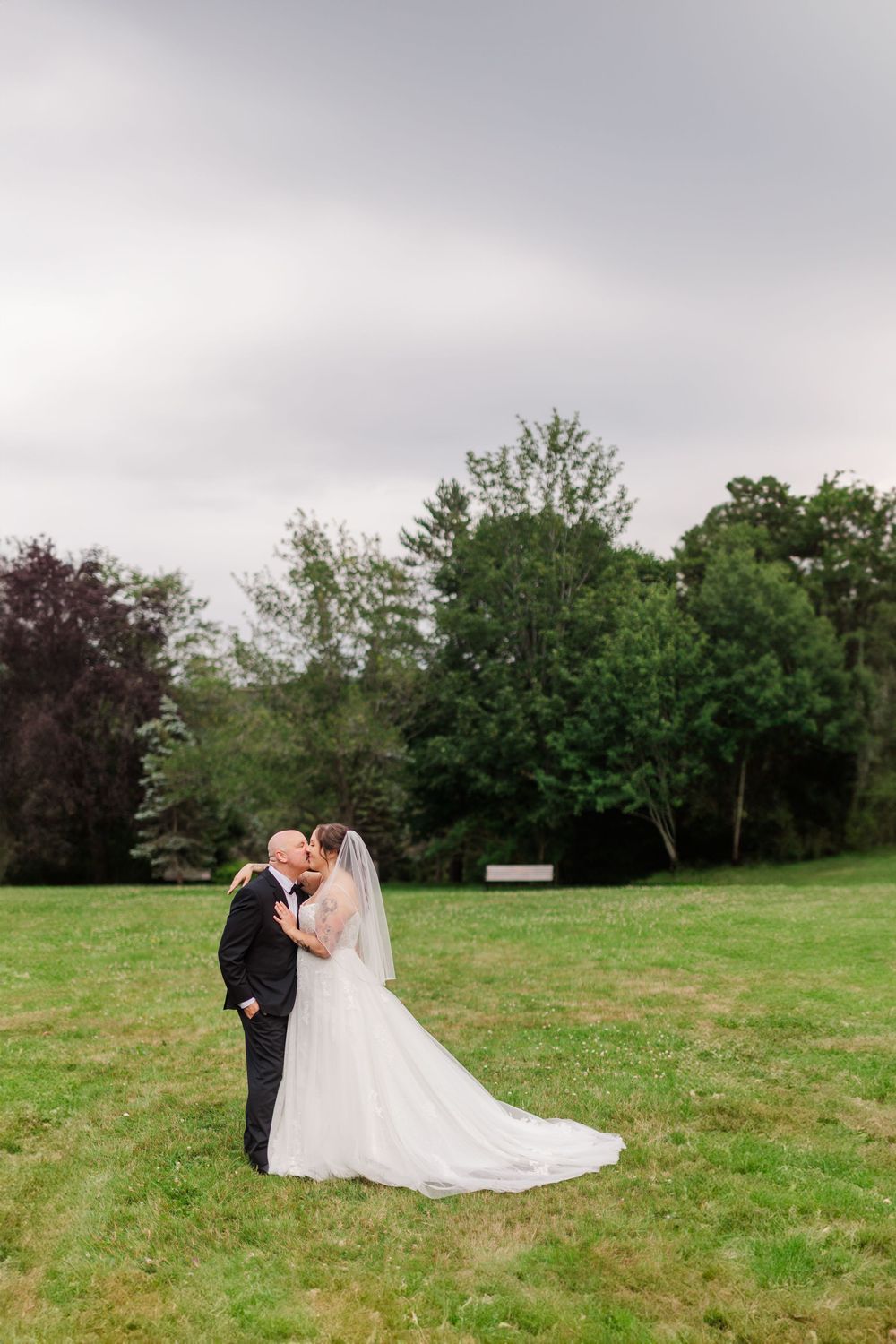 A bride and groom share a romantic kiss in a lush green field on their wedding day.