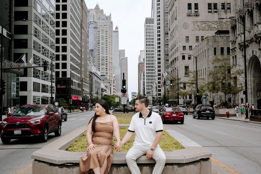 Couple holding hands sitting on a median on Michigan Avenue in Chicago with city skyscrapers in the background.