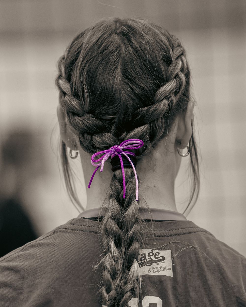 Close-up back view of a female athlete with braided hair tied with a purple ribbon bow.