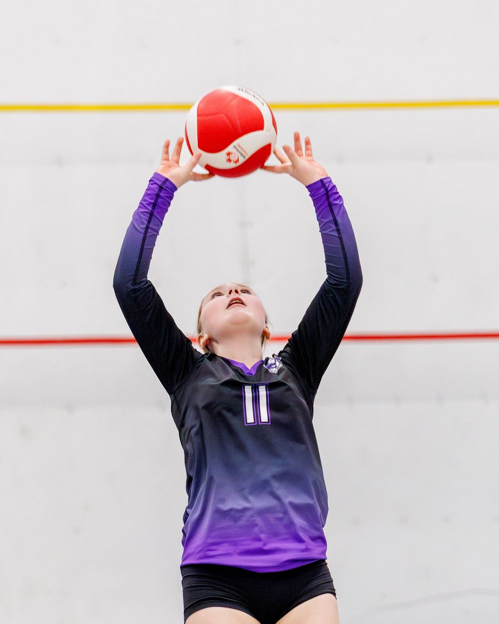 Female volleyball player in number 11 jersey setting a red and white ball overhead.