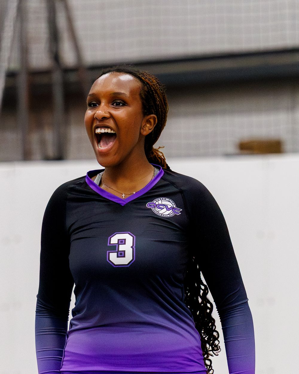 Smiling volleyball player wearing black and purple jersey number 3 during an indoor match.