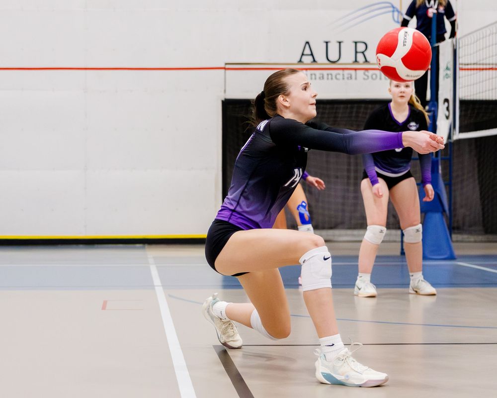 Female volleyball player digging a red and white ball during an indoor game.