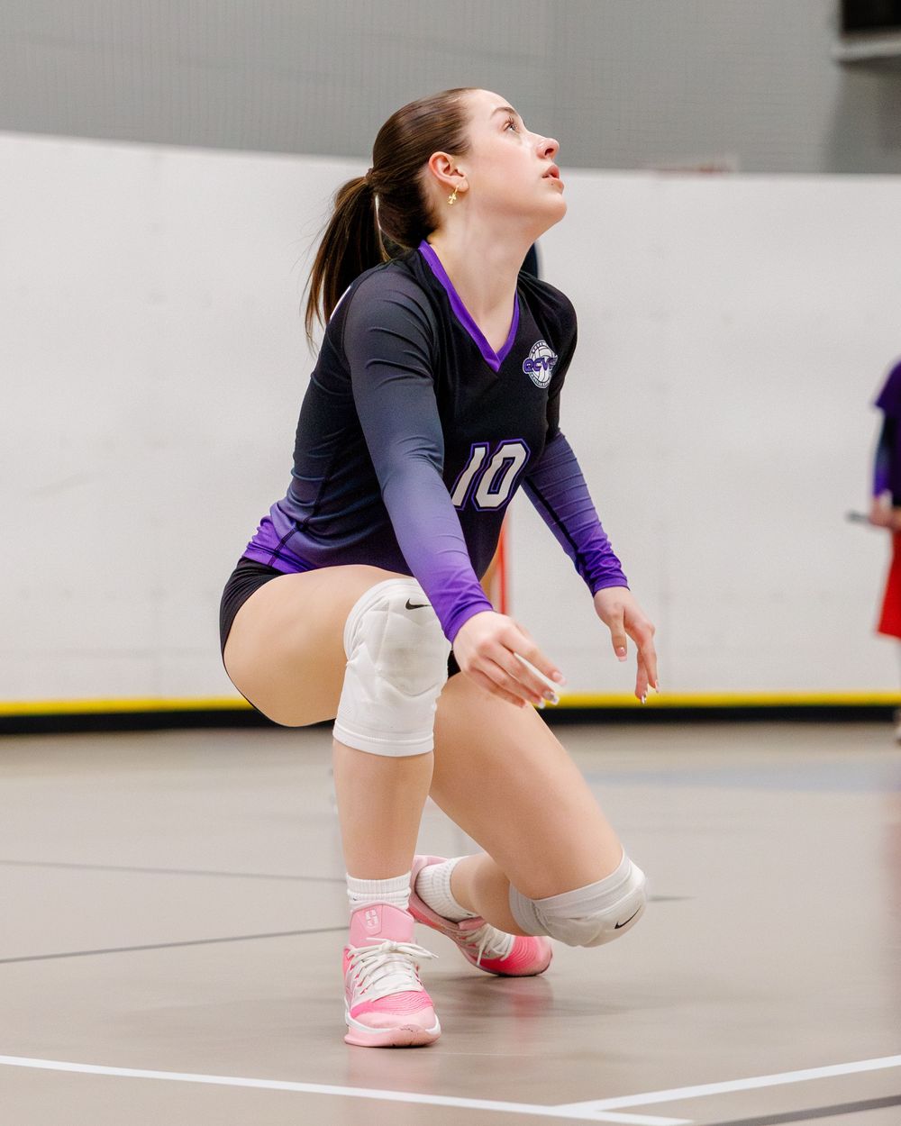 Volleyball player in black and purple number 10 jersey crouching low on indoor court.