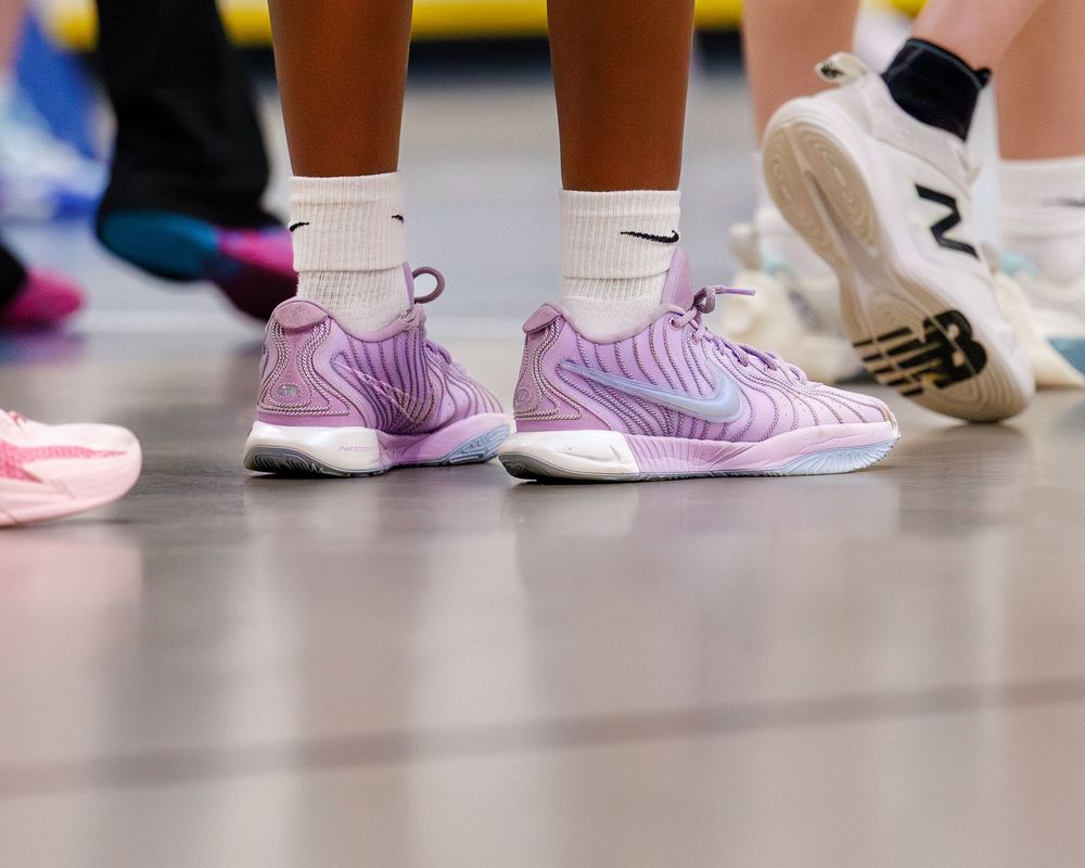 Close-up of athletes feet wearing purple Nike volleyball shoes on an indoor sports court.