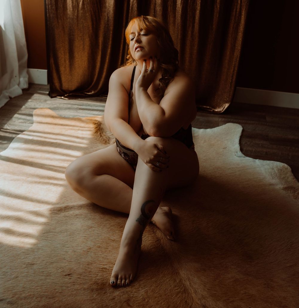 Wisconsin boudoir photoshoot of a woman in lingerie posing gracefully on a fur rug with warm sunlight streaming through curtains.
