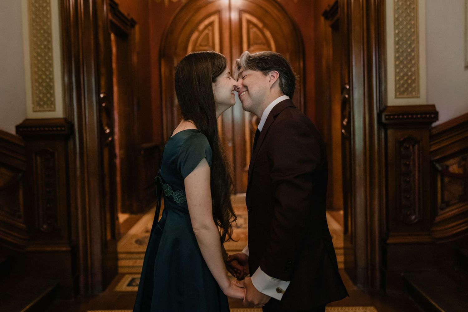 Couple sharing a romantic moment holding hands in an elegant hallway with ornate wooden doors.