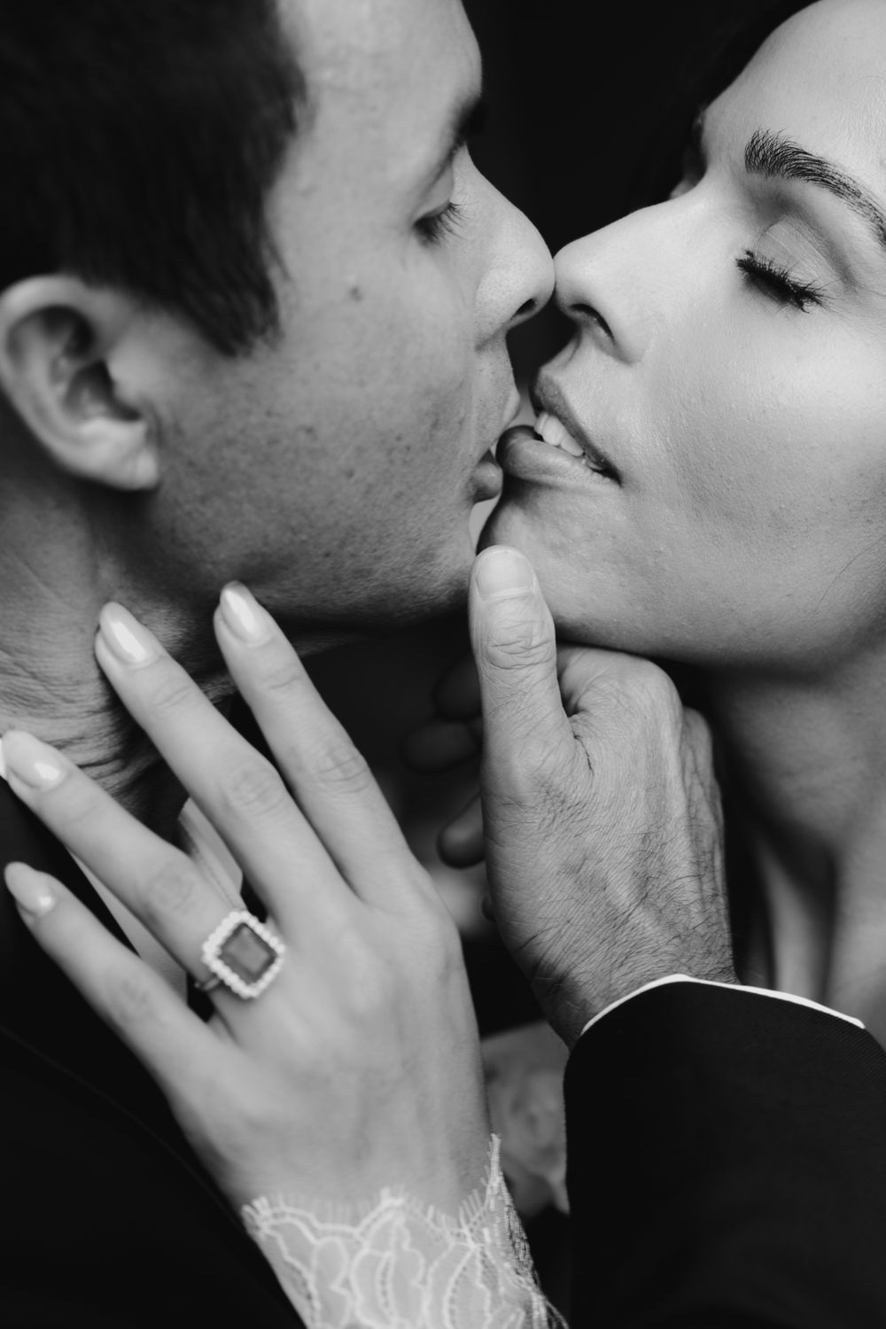 Black and white photo of a couple sharing a romantic kiss, bride wearing an elegant emerald-cut diamond engagement ring.