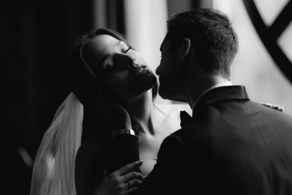 Black and white wedding photo of bride and groom sharing a romantic moment, with soft dramatic lighting.