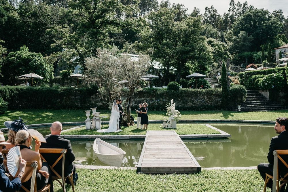 Outdoor wedding ceremony by a serene garden pond, with guests seated on wooden chairs amid lush greenery.