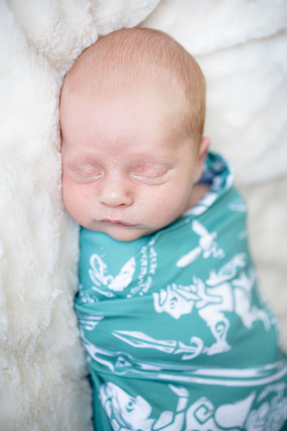 Sleeping newborn baby swaddled in a teal and white patterned blanket with medieval knight designs.