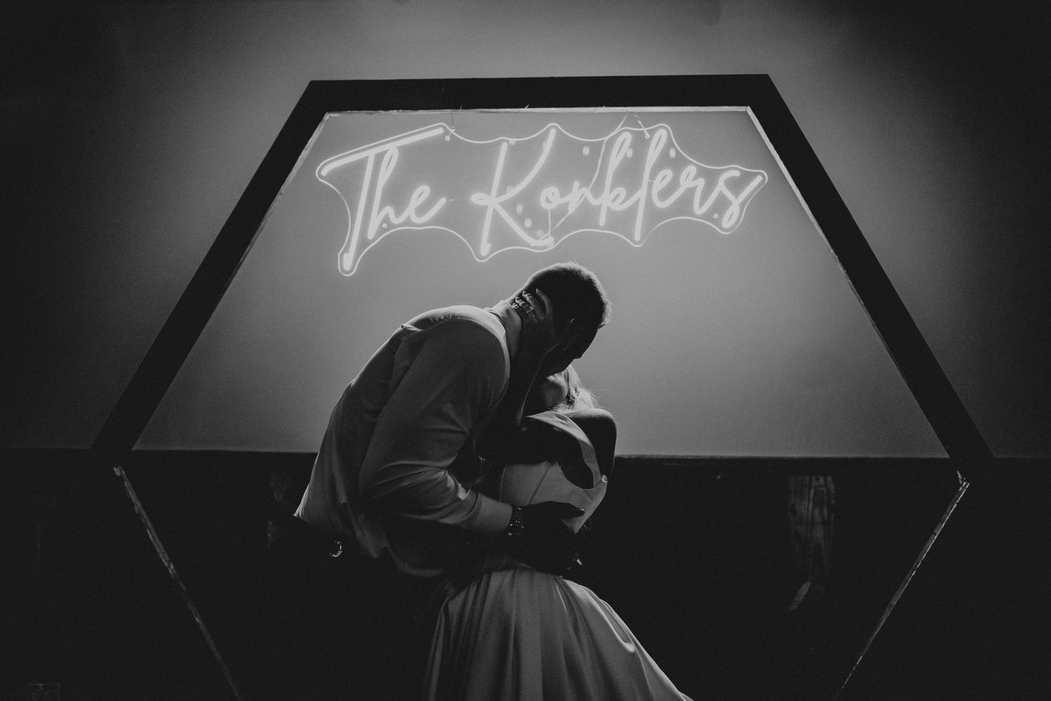 Black and white photo of a couple sharing a romantic embrace in front of a neon sign reading The Ranklers.