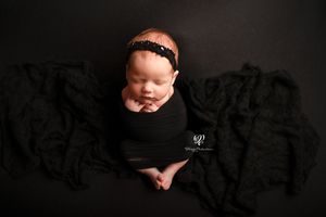 Newborn baby girl posed on black backdrop wrapped in black fabric; newborn photoshoot Lexington, SC; best photographer