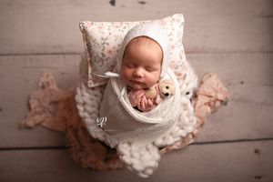 Newborn baby girl wrapped in white with bonnet holding teddy bear posed in basket on wood floor; newborn photographer SC