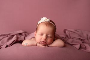 Baby pictures; newborn girl with flower headband posed head on hands with pink backdrop; newborn photographer Lexington