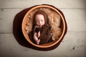 Baby newborn boy wrapped in brown with bonnet posed in bowl on wood floor; newborn session Lexington, SC