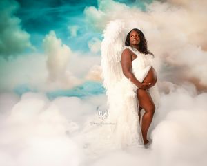 Black woman posed with wings on clouds in maternity photoshoot Lexington, SC; beautiful black pregnant woman professional photoshoot