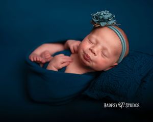 Luxury newborn photography Lexington, SC; jewel-tone newborn girl photoshoot; pursed lips wrapped in blue with flower headband
