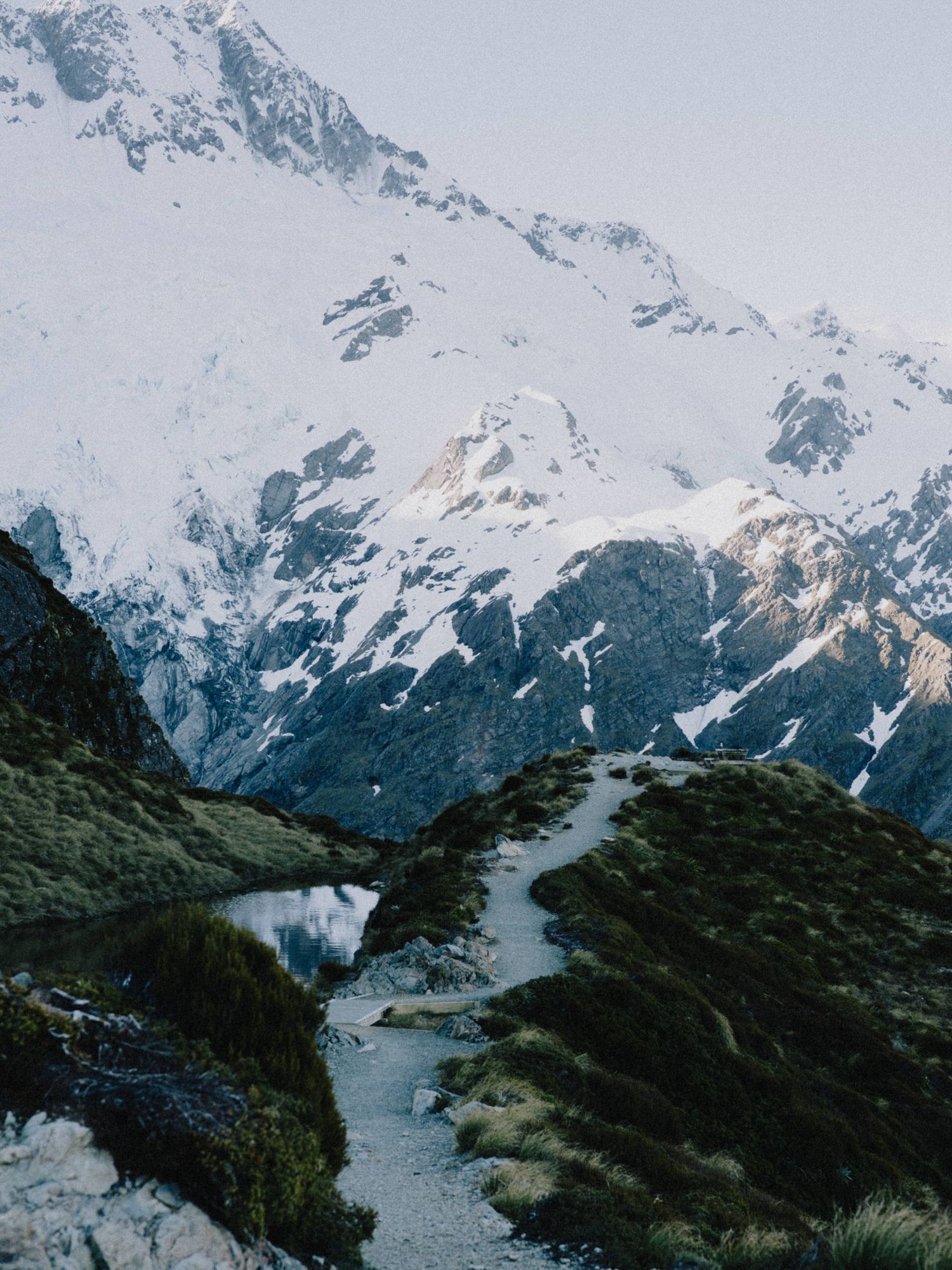 Snow-capped mountains tower over a winding path through rugged alpine terrain.