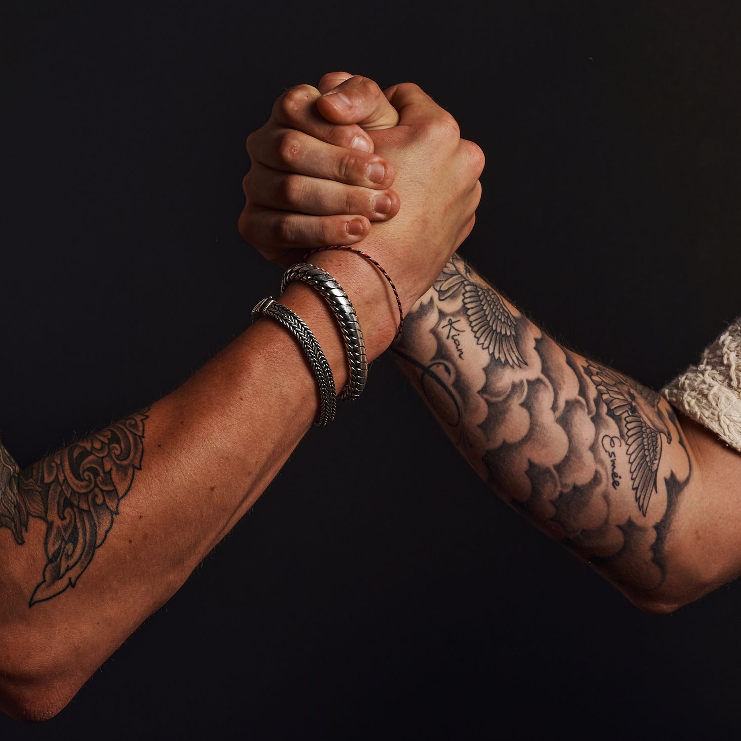 Close-up van twee getatoeëerde armen met een sterke handdruk.