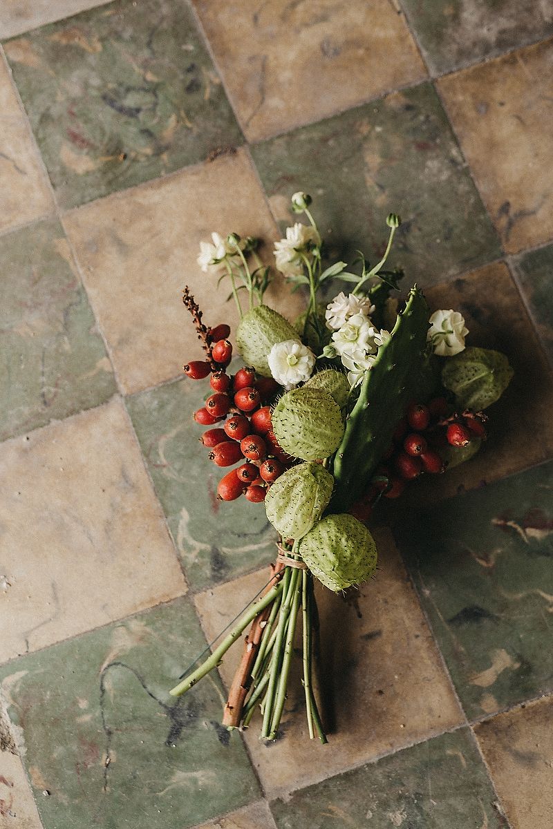 Rustic wedding bouquet with green pods, white flowers, and red berries on vintage tile floor during Riviera Maya wedding