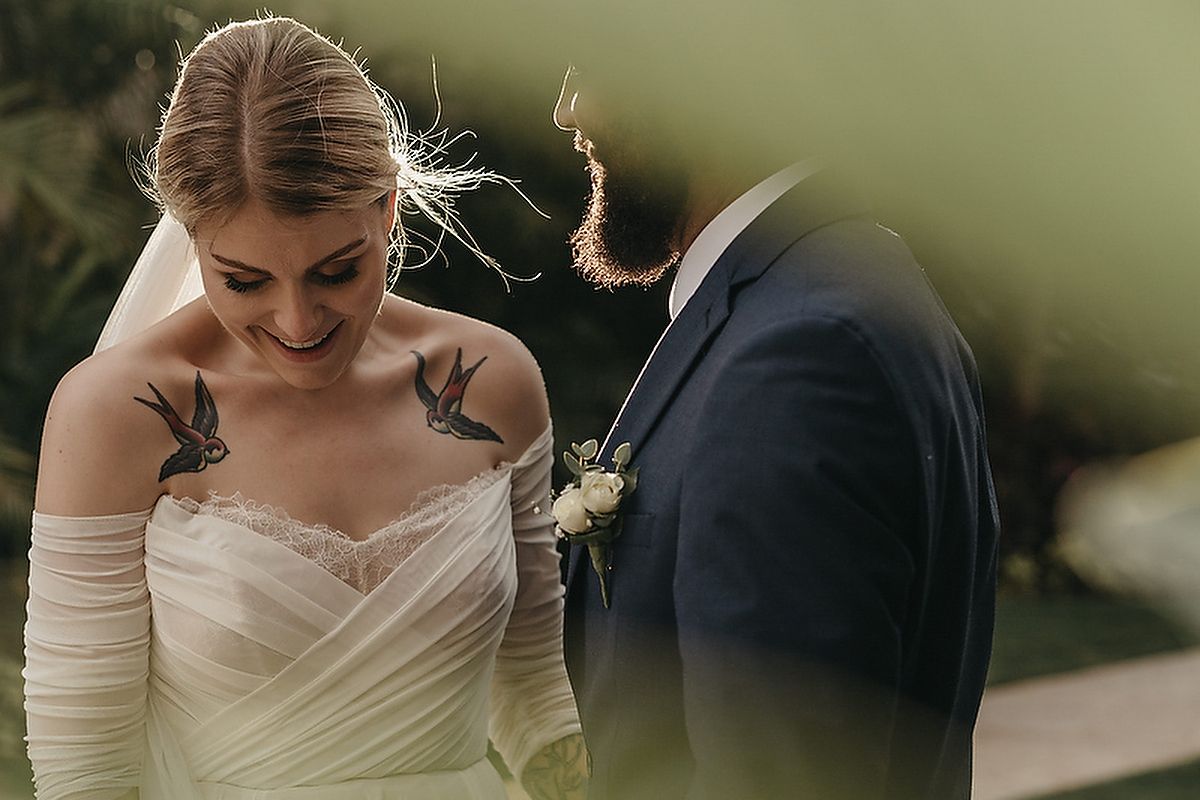 Bride with bird tattoos smiling at groom during intimate outdoor ceremony at Villa la Joya.