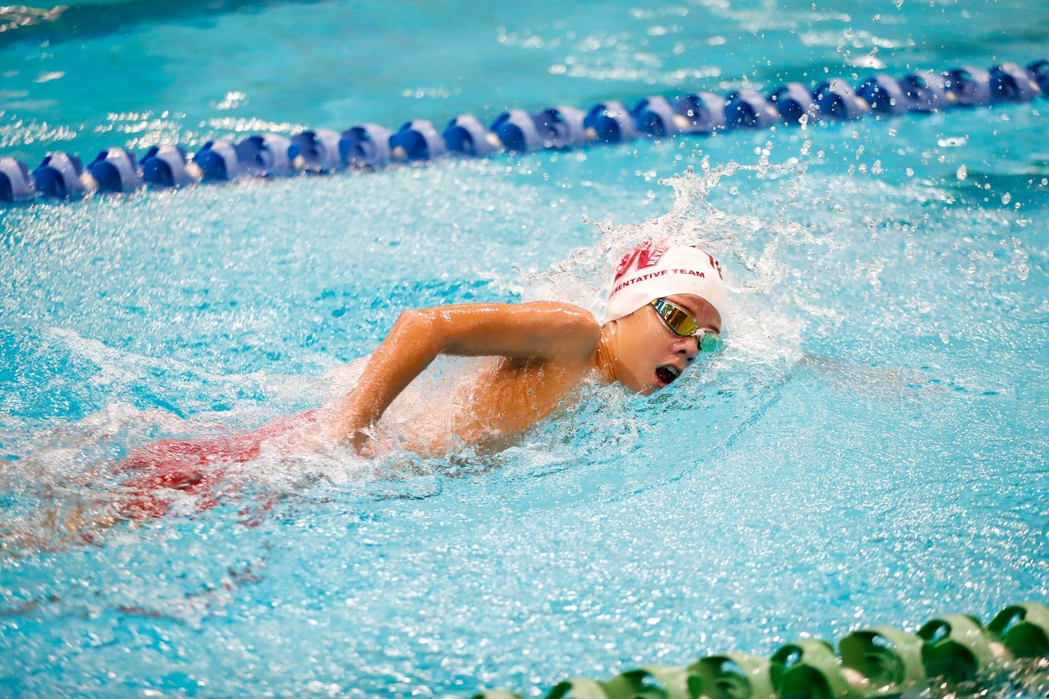 Swimmer performs freestyle stroke in pool during competitive race.