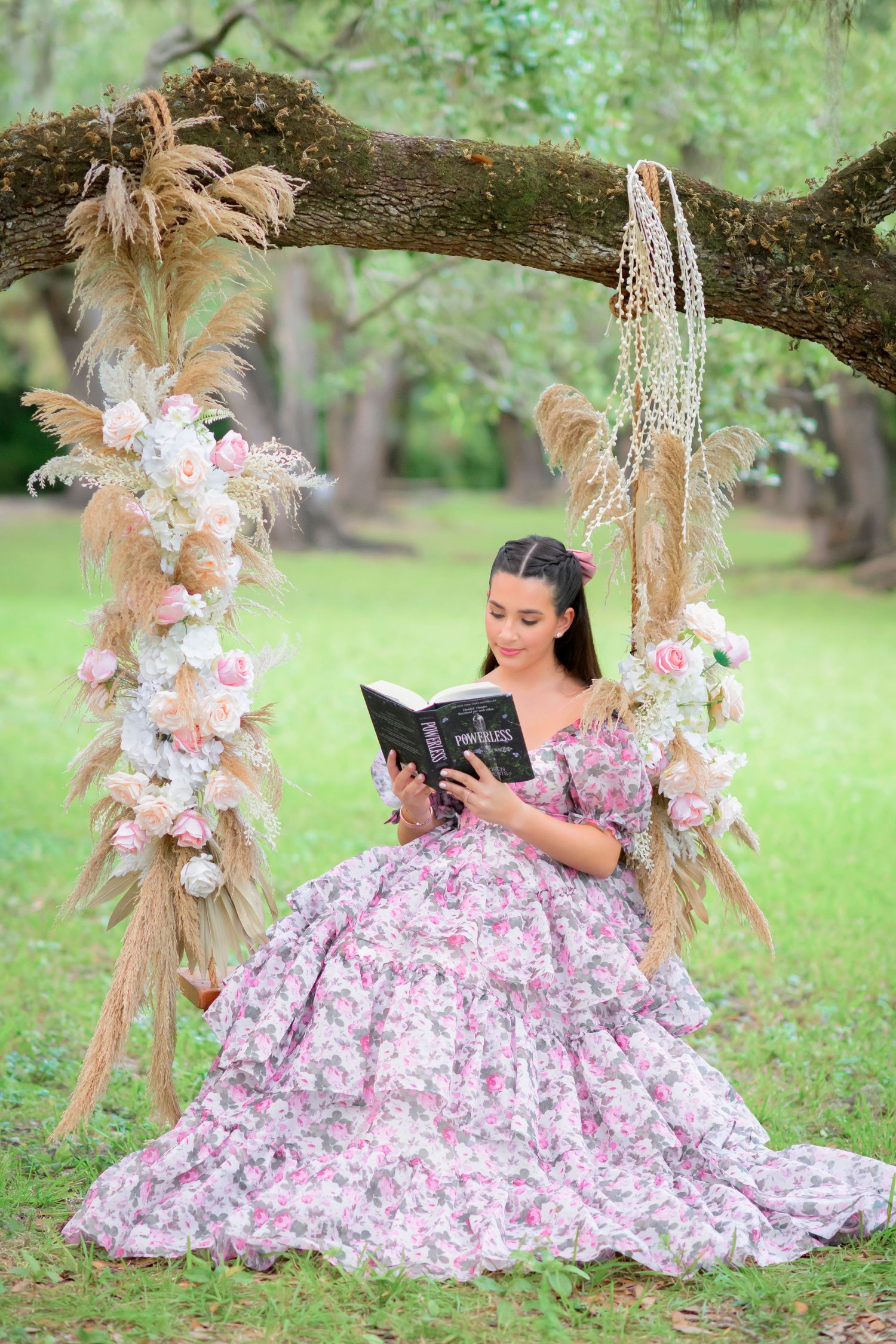 A girl reading in a romantic reading scene beneath a tree decorated with pampas grass, flowers and feathers in soft pink and beige tones.
