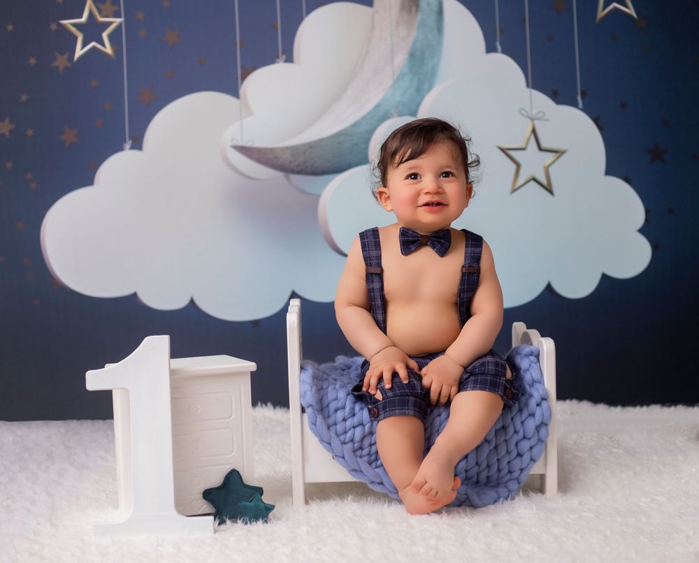 Navy blue starry backdrop with white clouds and hanging decorations for milestone photos.