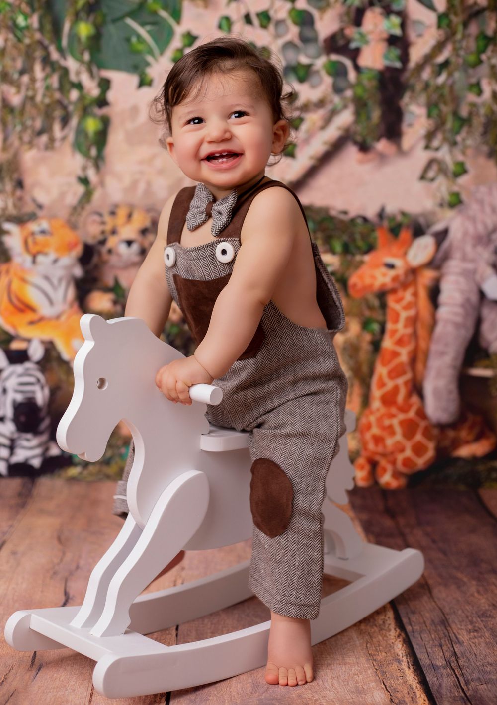 Toddler plays on white wooden rocking horse with floral background and plush toys.