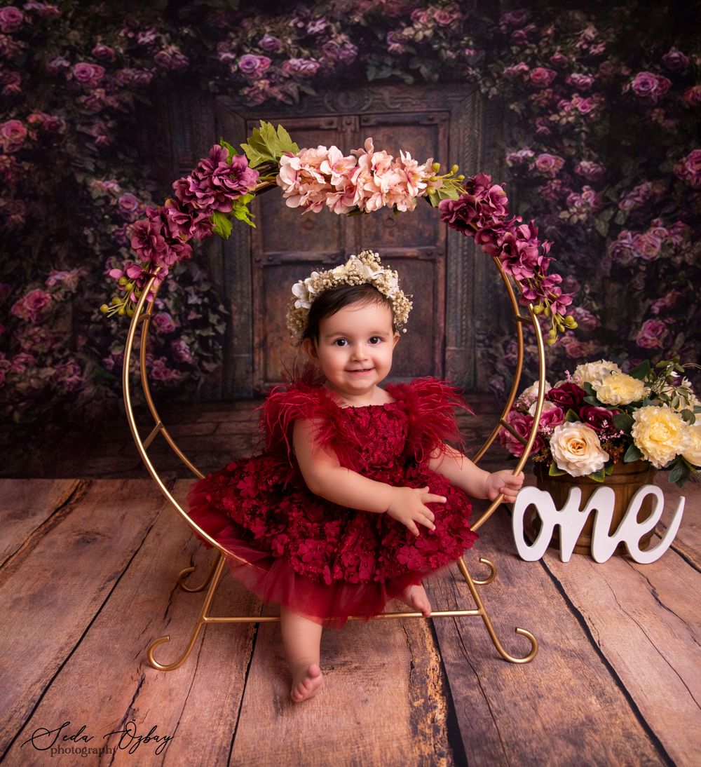 Baby milestone photos with cherry blossoms and red tulle dress on wooden floor.