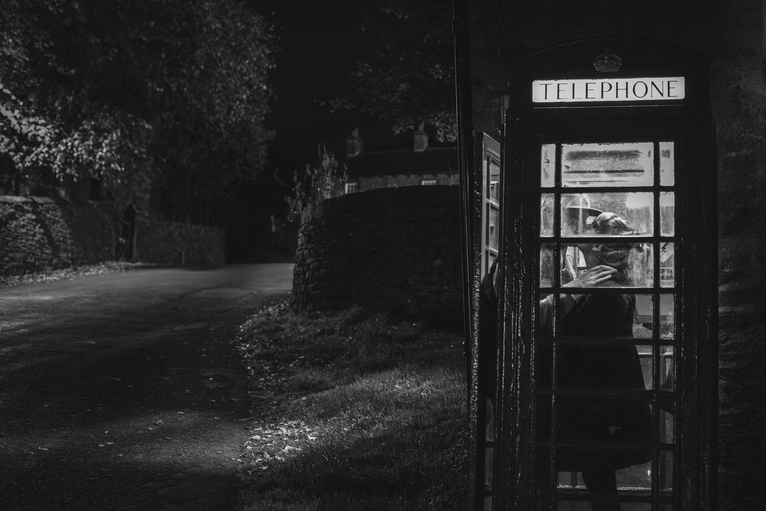 Moody black and white photograph of an illuminated phone booth at night.