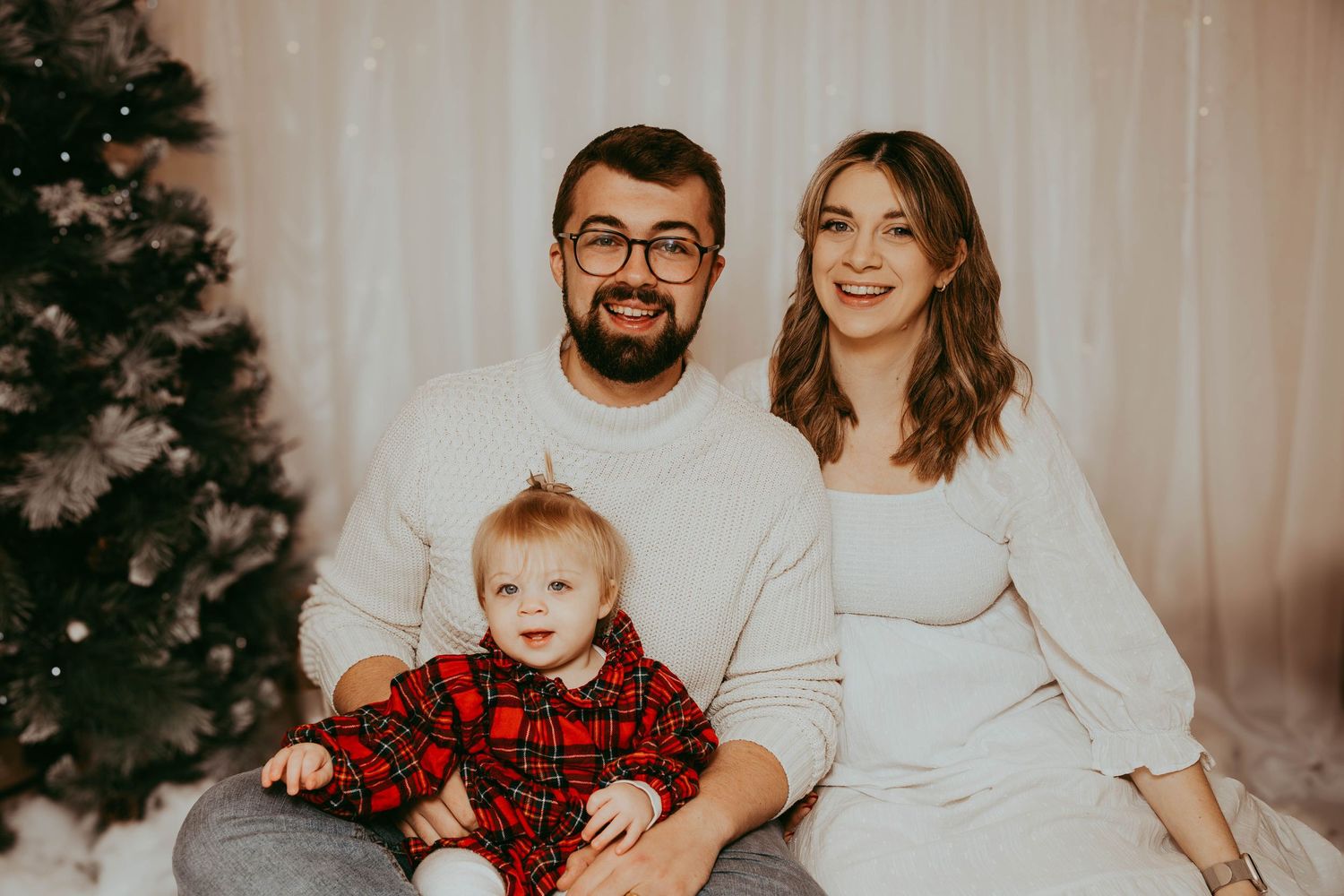 Indoor family Christmas portrait with plaid outfit accents and white backdrop.