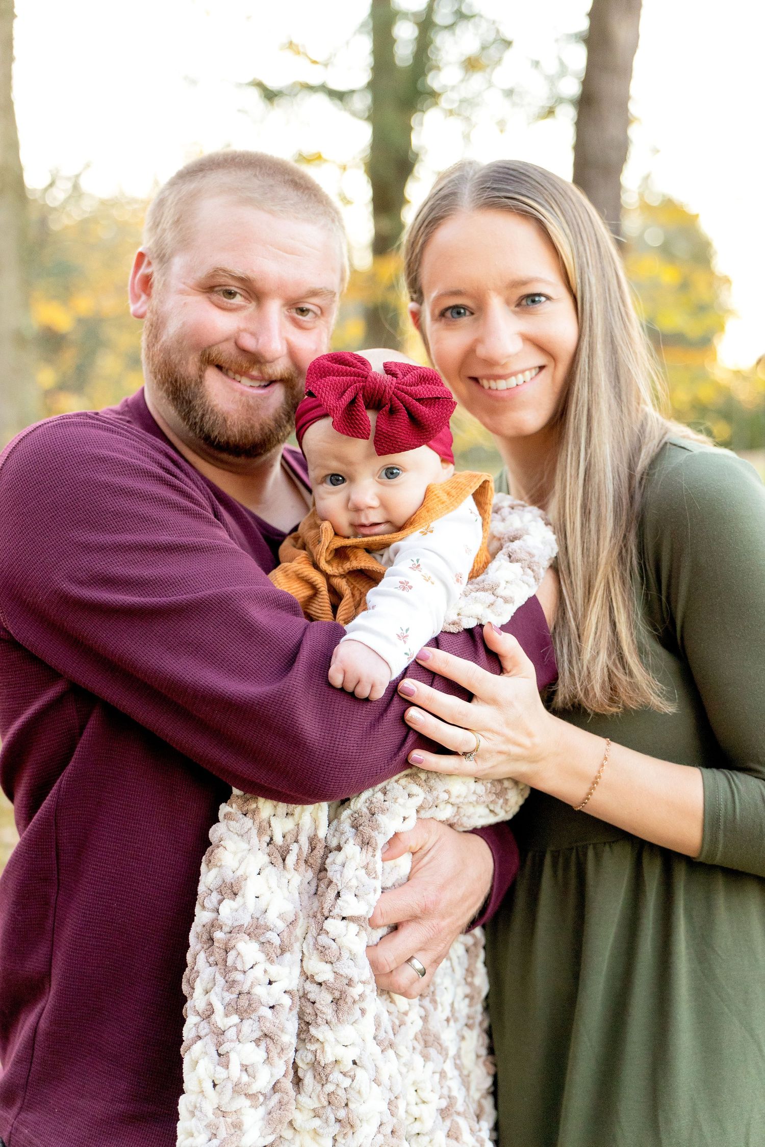 A family poses together outdoors during autumn, wearing burgundy and green.