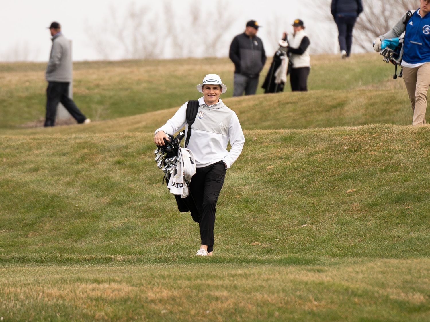 Golfer walks uphill carrying golf bag across winter course terrain.