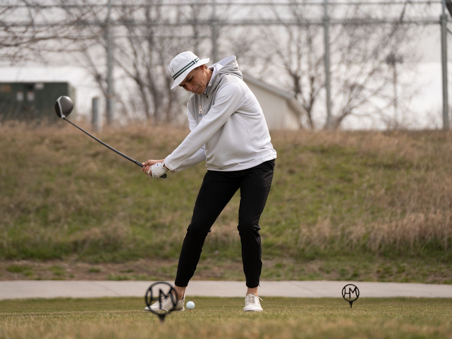 Golfer in white sweater takes a swing at driving range with practice balls.