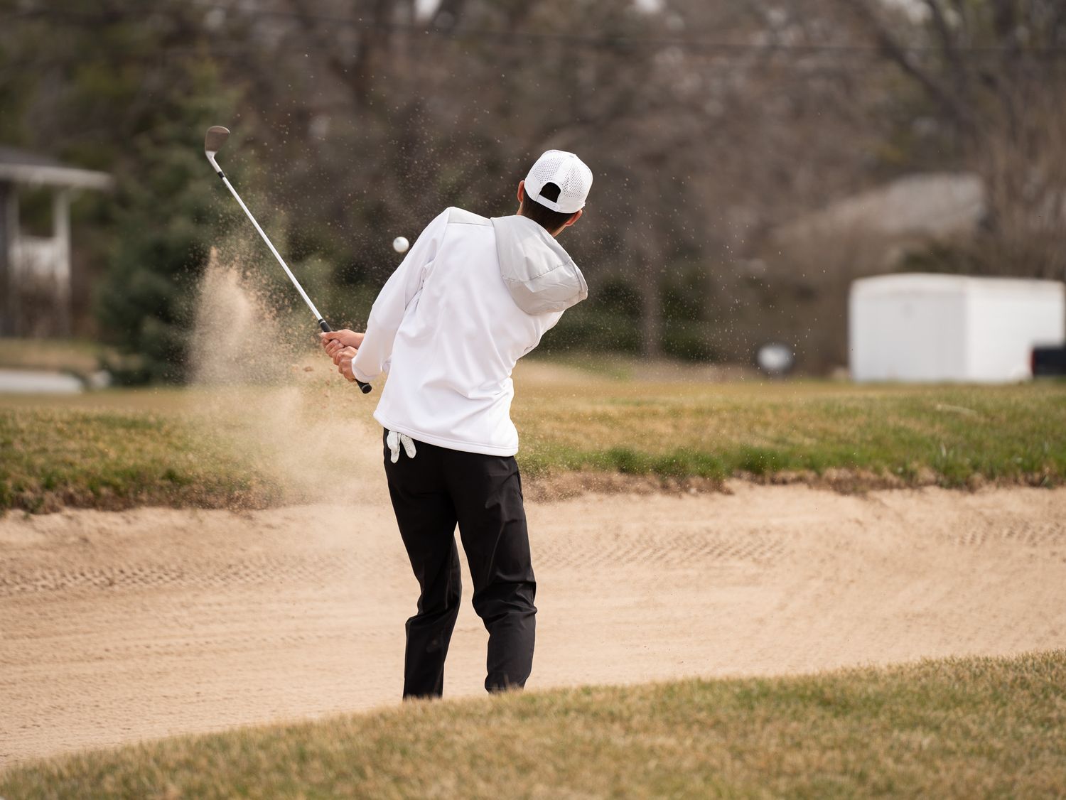 Golfer hits shot from bunker with perfect form on winter golf course.