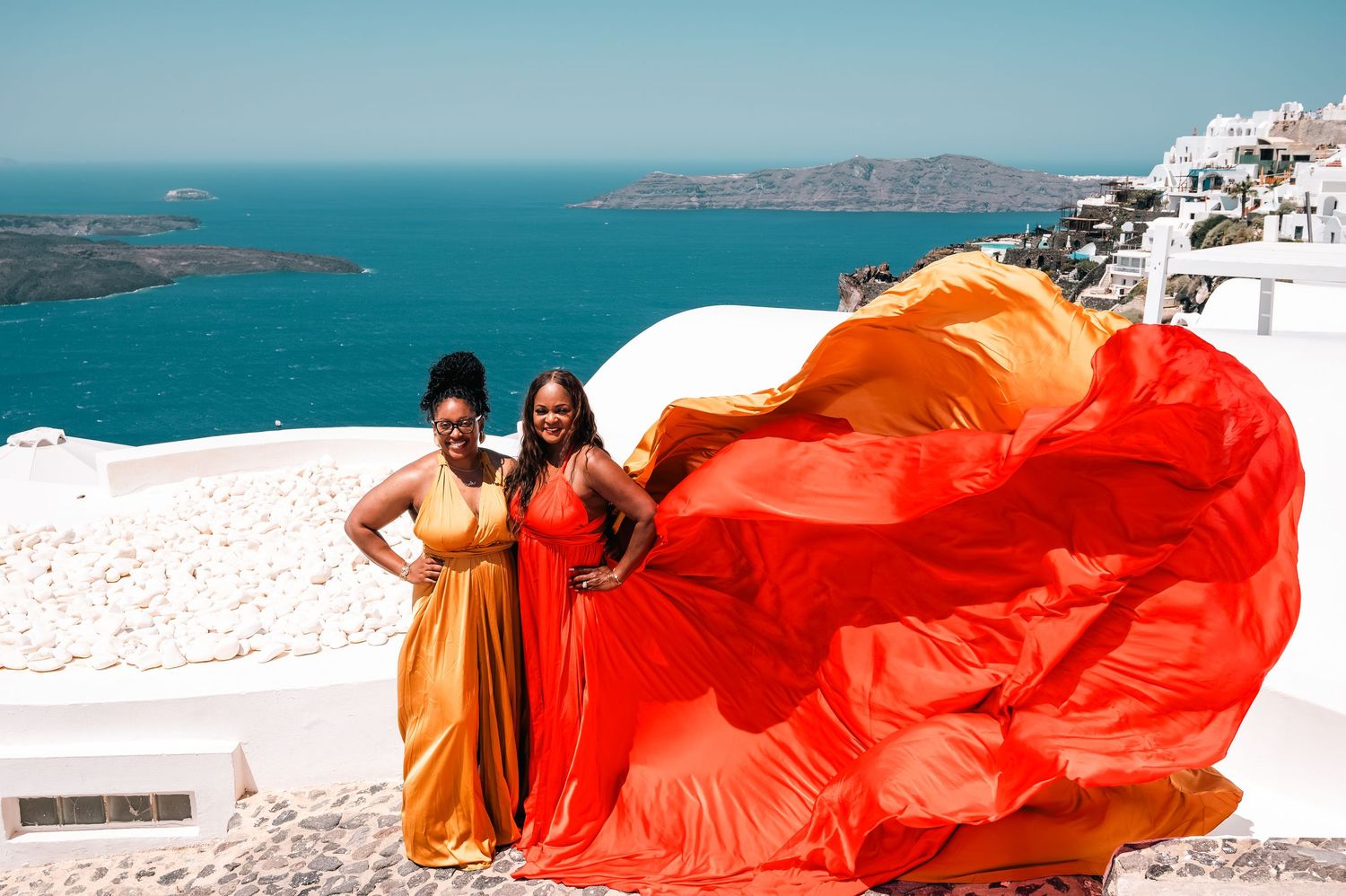 A dramatic red flowing dress contrasts against white walls and blue dome church in Santorini.